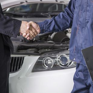 Ein Geschäftsmann gibt einem Automechaniker vor einer geöffneten Motorhaube die Hand, was eine erfolgreiche Servicevereinbarung symbolisiert.