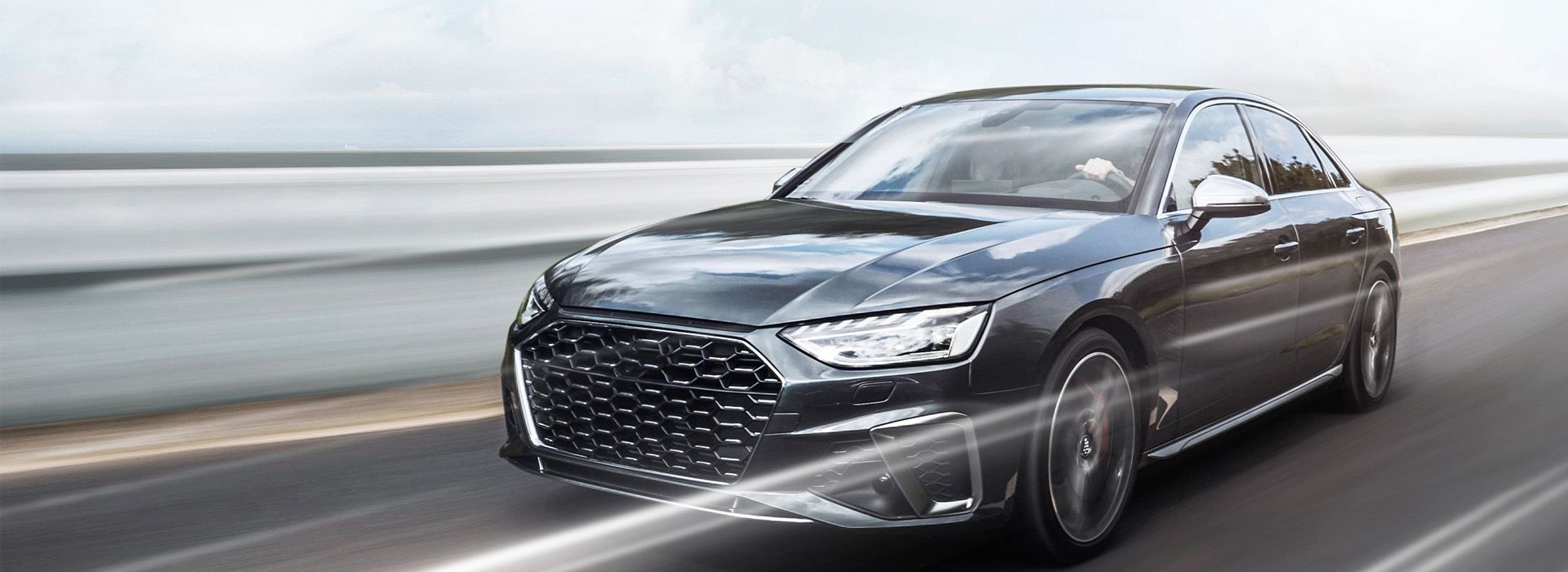 Eine elegante schwarze Limousine rast eine Küstenstraße entlang, ihr modernes Design wird durch einen stilvollen Kühlergrill und dynamische Bewegungsunschärfe unterstrichen.